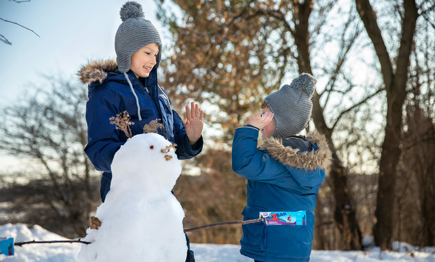 Two kids with a snowman, eating a CLIF KID zBar